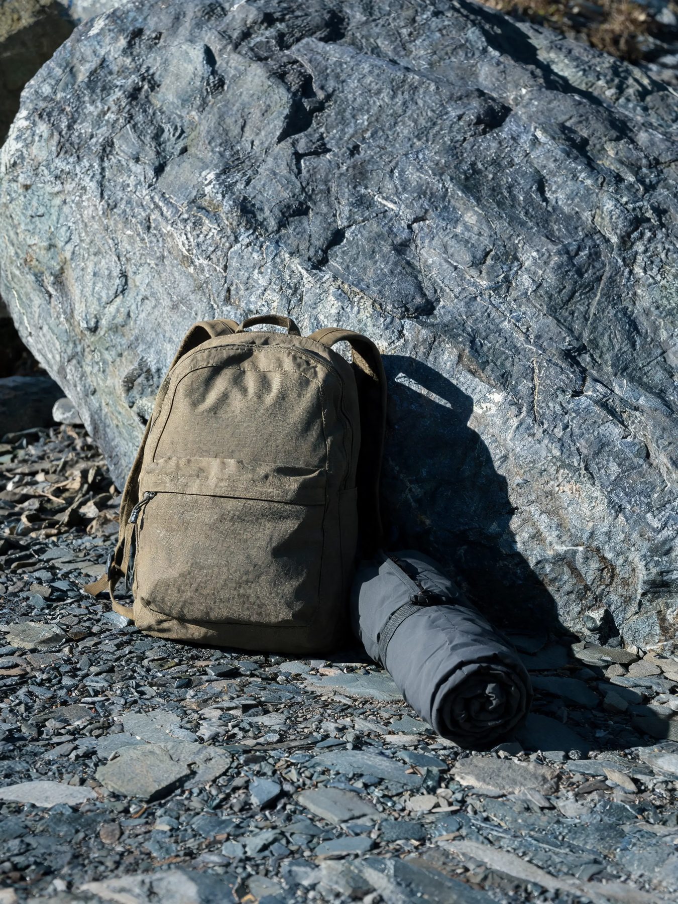 Ripstop daypack and rolled shell jacket against a slate boulder