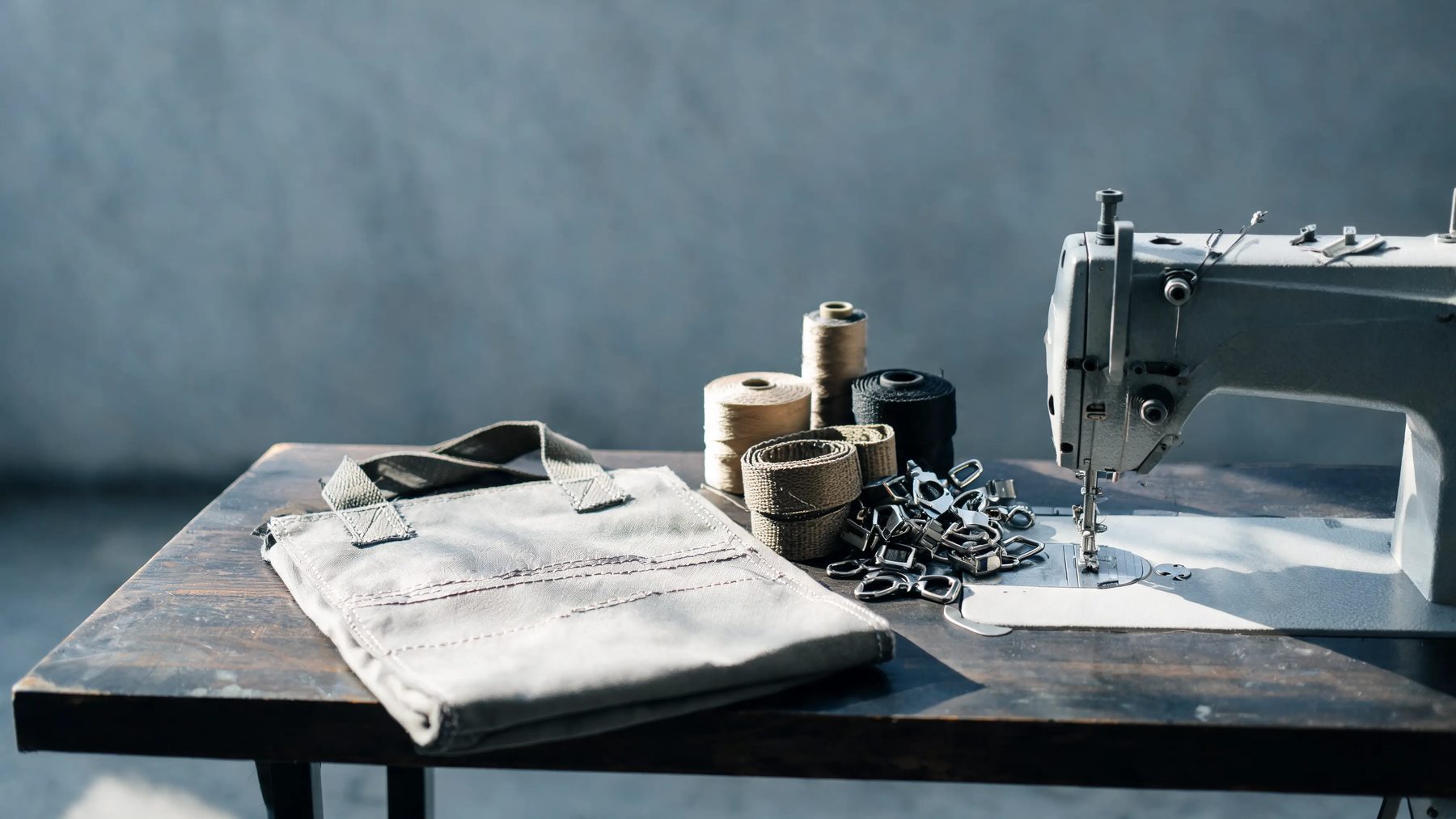 Workshop table with a half-stitched pack panel, webbing spools and buckles